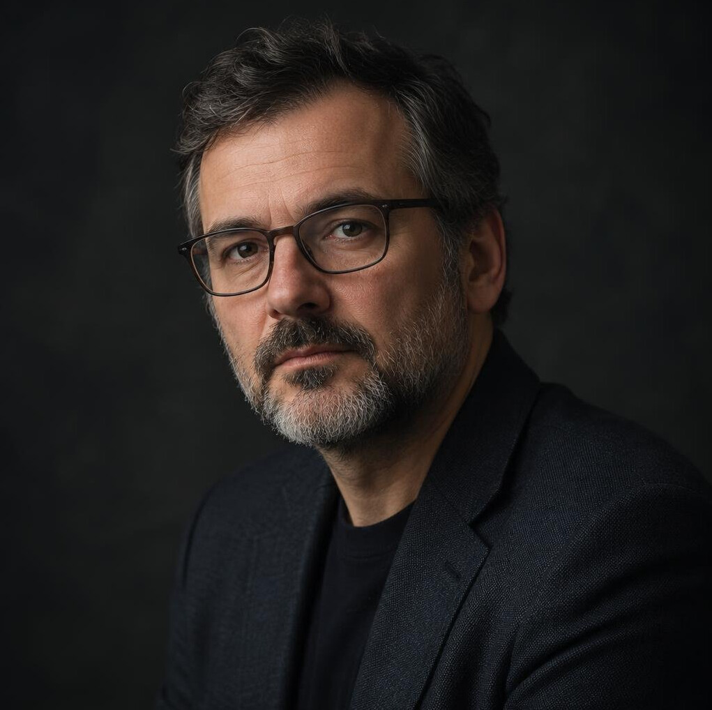Studijski portret sredovječnog muškarca s bradom i naočalama u tamnom sakou